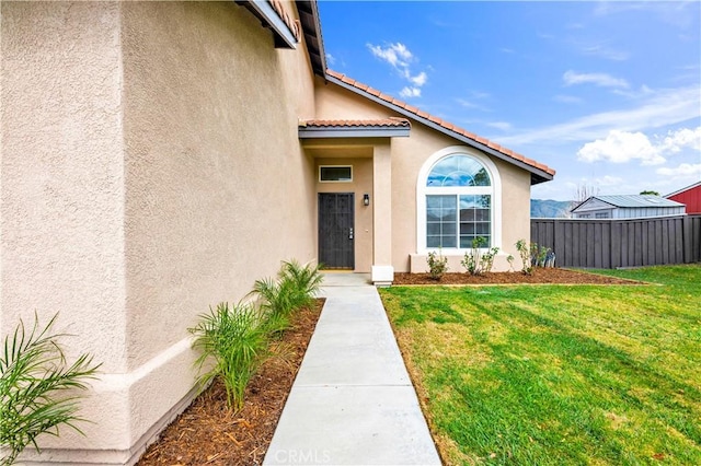 doorway to property with a tiled roof, stucco siding, a lawn, and fence