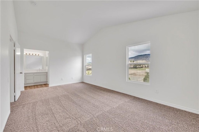 unfurnished bedroom featuring baseboards, ensuite bath, lofted ceiling, light colored carpet, and a mountain view