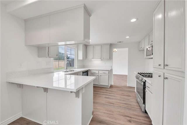 kitchen with a breakfast bar, light wood-style flooring, a sink, stainless steel appliances, and a peninsula