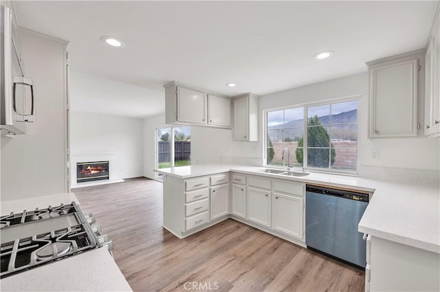 kitchen with a sink, a peninsula, light wood finished floors, dishwasher, and light countertops