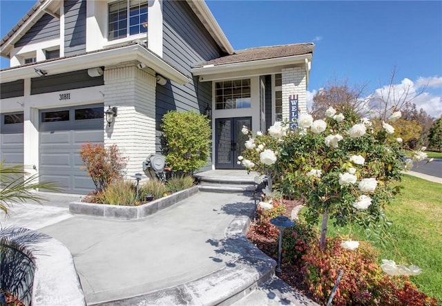 view of exterior entry featuring french doors, brick siding, and a garage