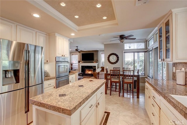 kitchen featuring a tray ceiling, ornamental molding, decorative backsplash, recessed lighting, and appliances with stainless steel finishes