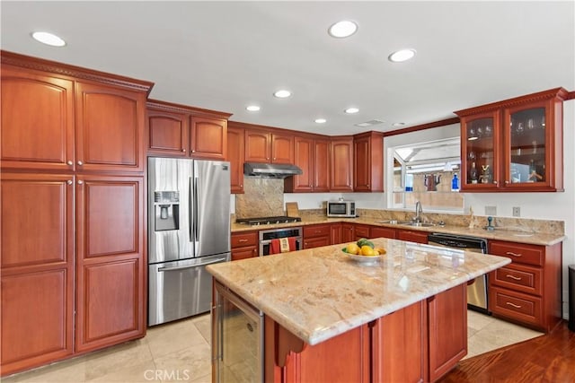 kitchen with a sink, light stone countertops, under cabinet range hood, and stainless steel appliances