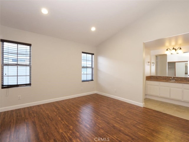 empty room featuring a sink, wood finished floors, recessed lighting, baseboards, and vaulted ceiling