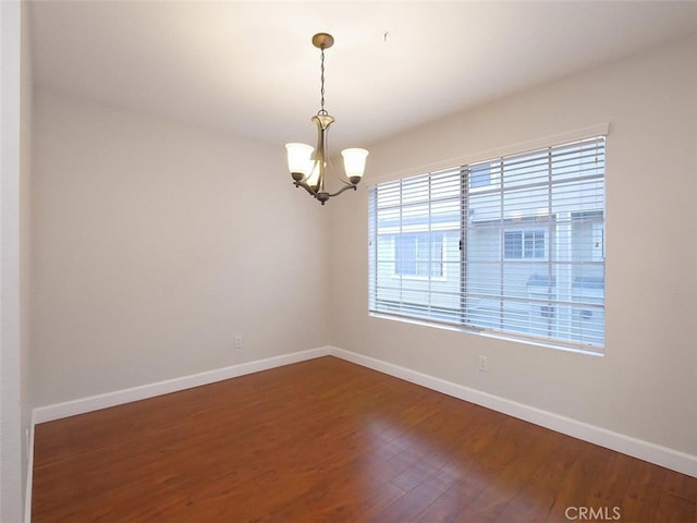 spare room featuring a notable chandelier, dark wood-type flooring, and baseboards