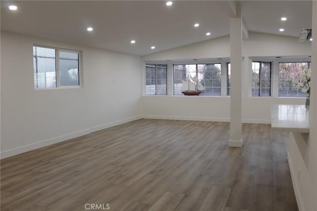 empty room featuring plenty of natural light, wood finished floors, baseboards, and vaulted ceiling