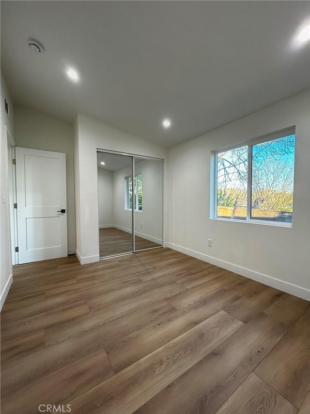 unfurnished bedroom featuring recessed lighting, a closet, baseboards, and wood finished floors