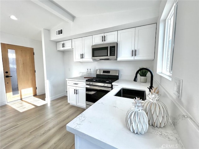 kitchen featuring visible vents, vaulted ceiling with beams, appliances with stainless steel finishes, white cabinetry, and a sink