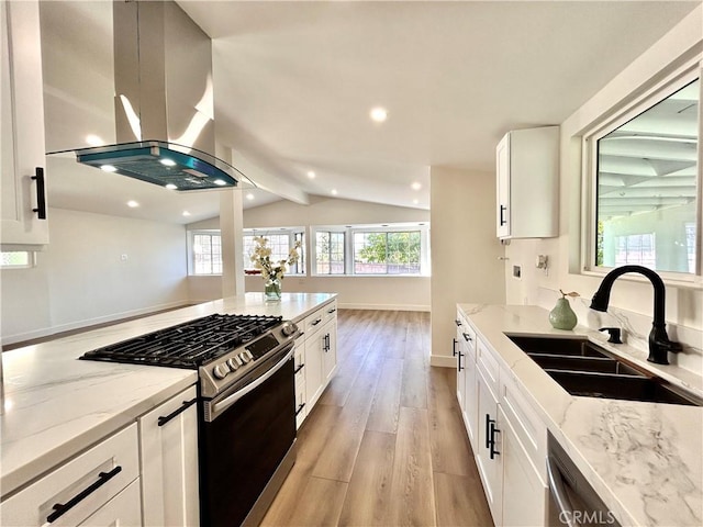 kitchen featuring light wood-type flooring, light stone counters, island exhaust hood, stainless steel gas stove, and a sink