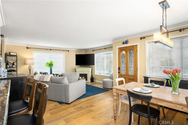 living area featuring light wood-type flooring, baseboards, a lit fireplace, and crown molding