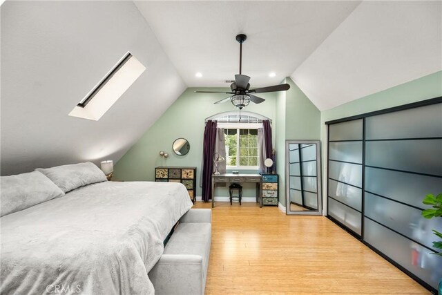 bedroom featuring vaulted ceiling with skylight, baseboards, a ceiling fan, and wood finished floors