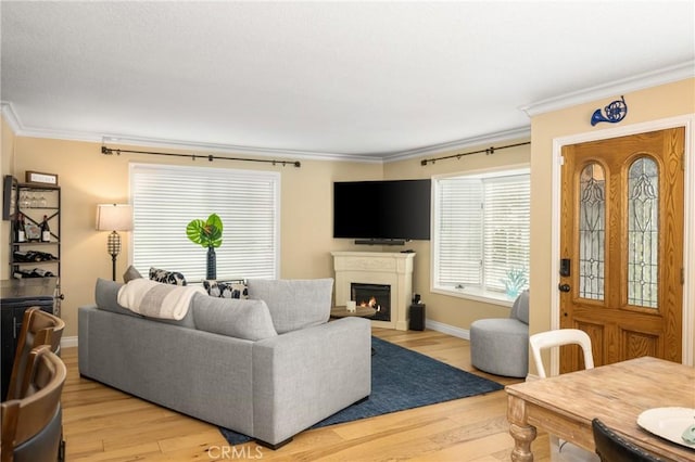 living area featuring light wood finished floors, a warm lit fireplace, baseboards, and ornamental molding