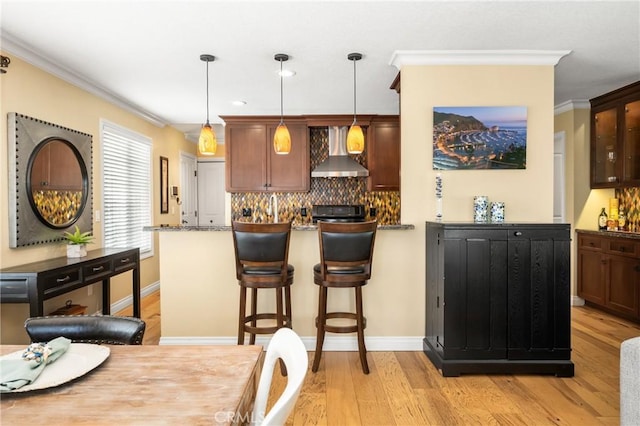 kitchen with decorative backsplash, hanging light fixtures, light wood-style floors, crown molding, and wall chimney exhaust hood