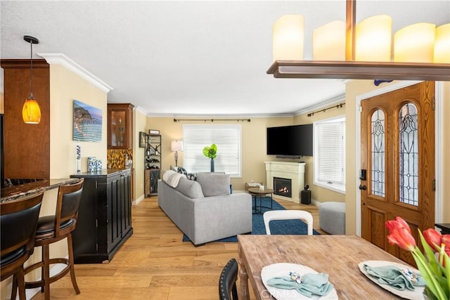 living room with baseboards, a warm lit fireplace, ornamental molding, and light wood finished floors