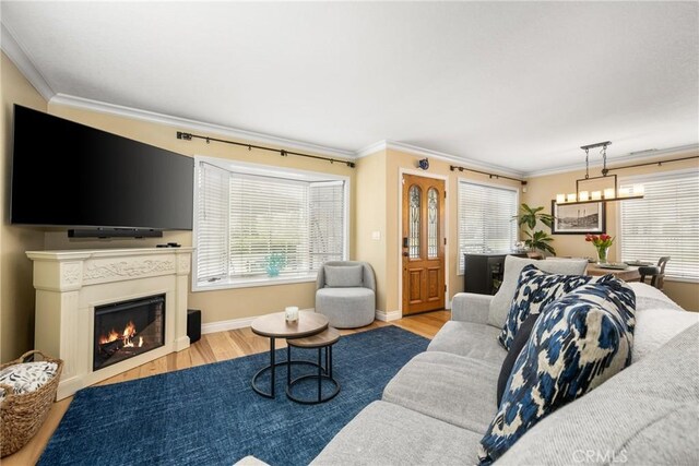 living room featuring a warm lit fireplace, wood finished floors, and crown molding