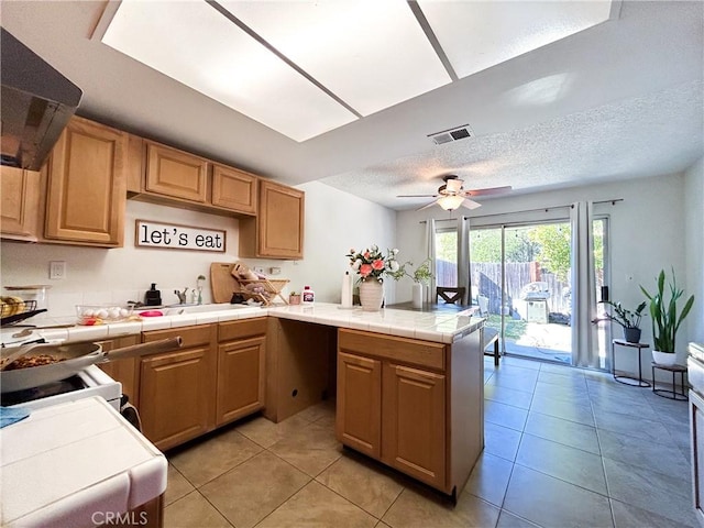 kitchen featuring visible vents, a textured ceiling, tile countertops, a peninsula, and extractor fan