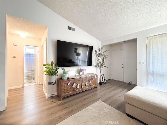 living area featuring vaulted ceiling, wood finished floors, visible vents, and a textured ceiling