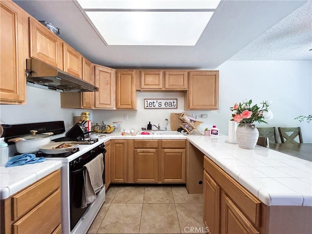 kitchen featuring under cabinet range hood, a sink, tile countertops, a peninsula, and gas range