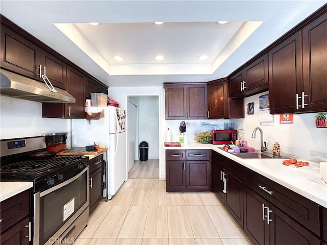 kitchen featuring stainless steel gas stove, under cabinet range hood, a sink, light countertops, and a raised ceiling