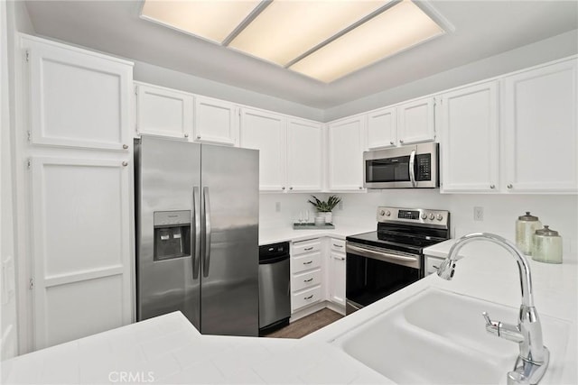 kitchen with a sink, stainless steel appliances, white cabinetry, and light countertops