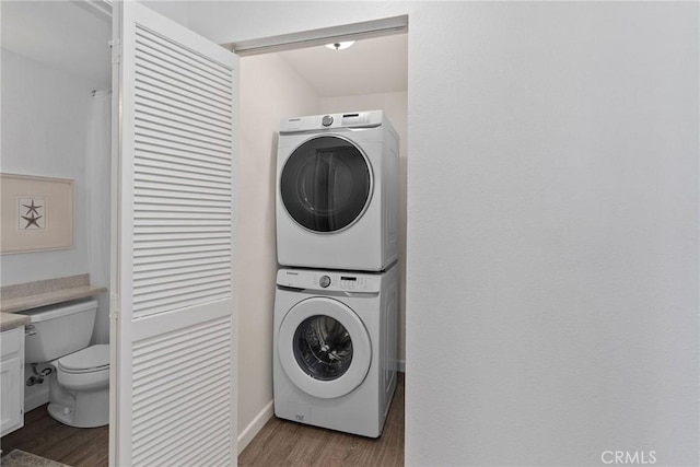 clothes washing area with stacked washer / dryer, laundry area, and wood finished floors