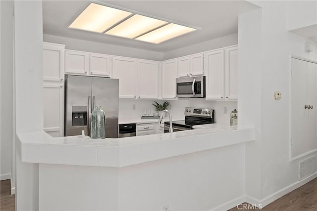 kitchen with visible vents, wood finished floors, stainless steel appliances, white cabinets, and baseboards