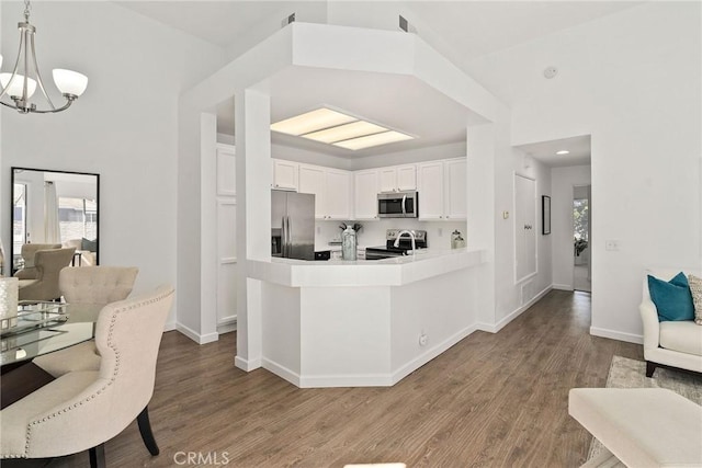 kitchen featuring wood finished floors, appliances with stainless steel finishes, white cabinetry, open floor plan, and a chandelier