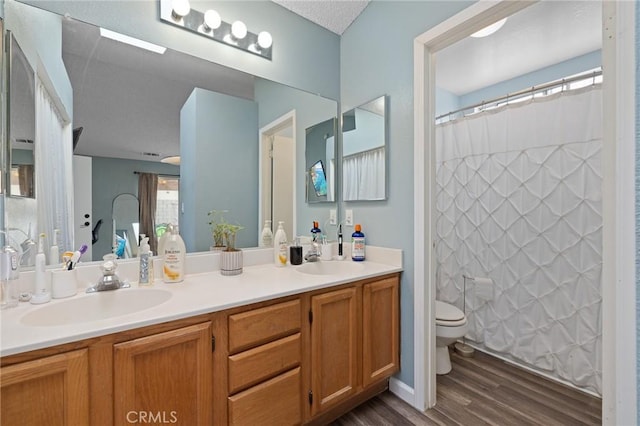 bathroom with double vanity, wood finished floors, toilet, and a sink