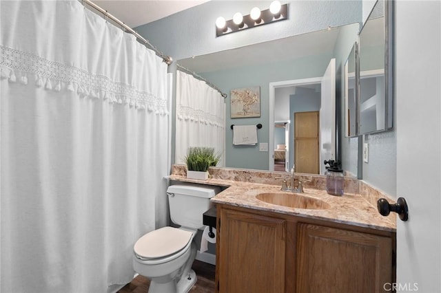 full bathroom featuring toilet, vanity, and a textured wall