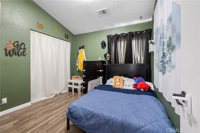 bedroom featuring visible vents, a textured ceiling, wood finished floors, baseboards, and lofted ceiling