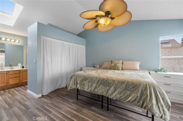 bedroom featuring baseboards, lofted ceiling with skylight, ensuite bathroom, wood finished floors, and a textured ceiling