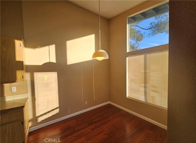 unfurnished room featuring dark wood-style floors, a textured ceiling, baseboards, and vaulted ceiling