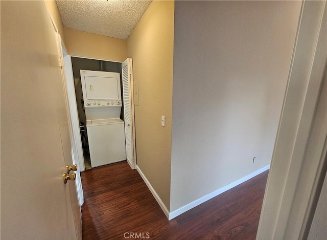 hallway with a textured ceiling, baseboards, dark wood-style flooring, and stacked washing maching and dryer