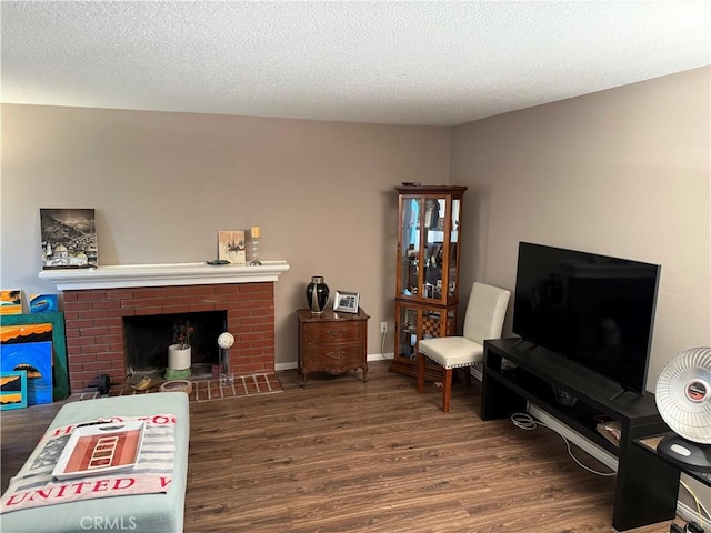 living room featuring a brick fireplace, a textured ceiling, baseboards, and wood finished floors