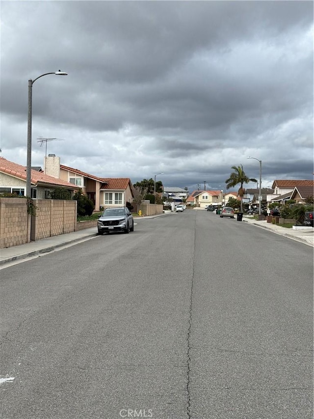 view of road with sidewalks, a residential view, curbs, and street lighting