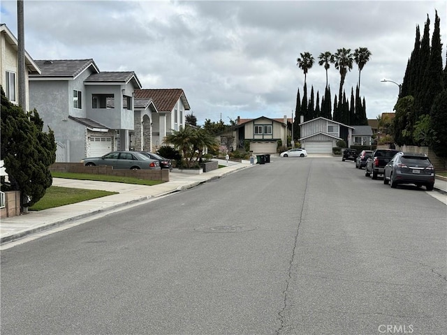 view of road with sidewalks, a residential view, curbs, and street lighting