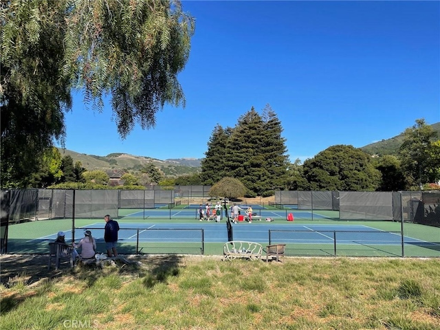 view of tennis court with a mountain view and fence