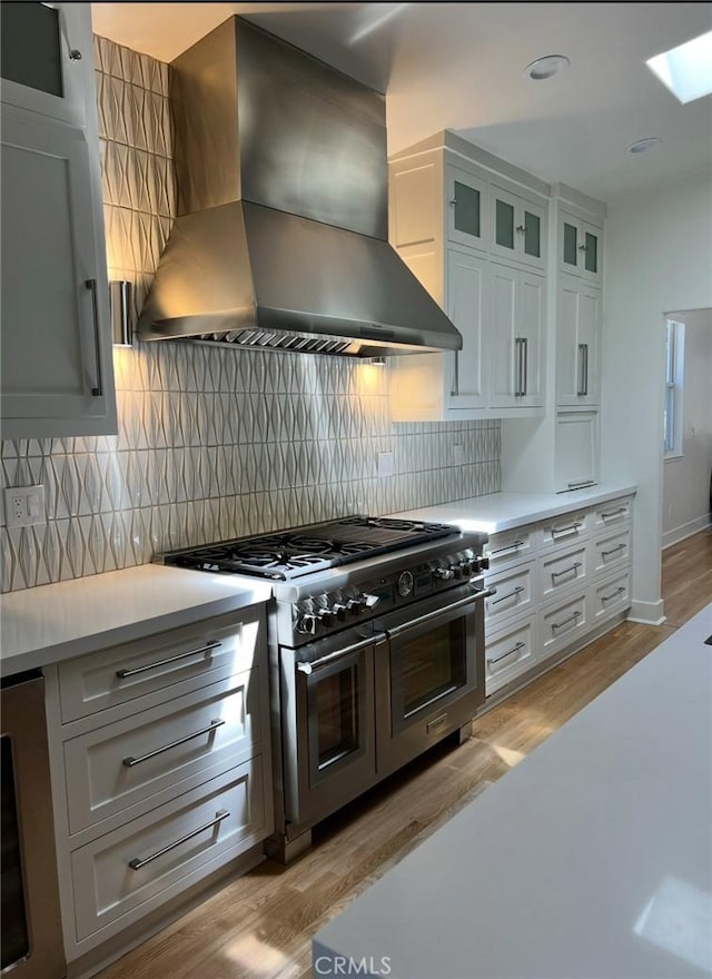 kitchen with range with two ovens, decorative backsplash, light countertops, light wood-style floors, and wall chimney range hood