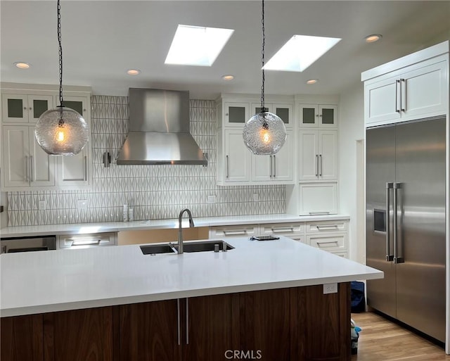 kitchen featuring stainless steel built in fridge, a skylight, wall chimney range hood, and a sink