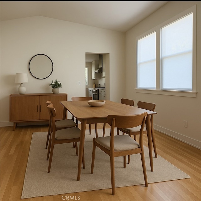 dining room with baseboards, light wood-type flooring, and lofted ceiling