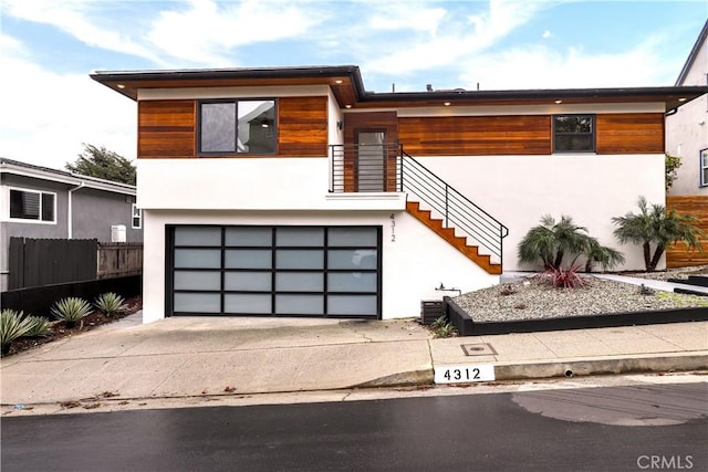 modern home with stucco siding, an attached garage, concrete driveway, and fence