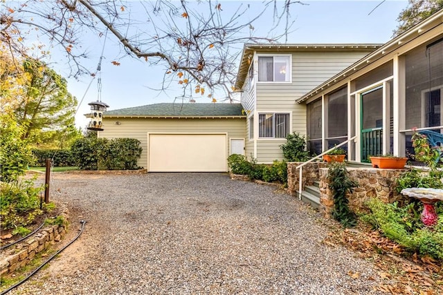 view of front of home featuring an attached garage, gravel driveway, and a sunroom