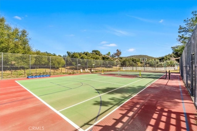 view of tennis court featuring community basketball court, a mountain view, and fence