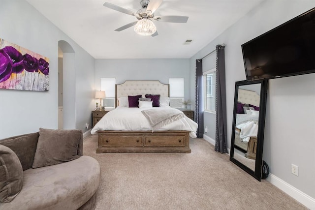 carpeted bedroom featuring ceiling fan, arched walkways, visible vents, and baseboards