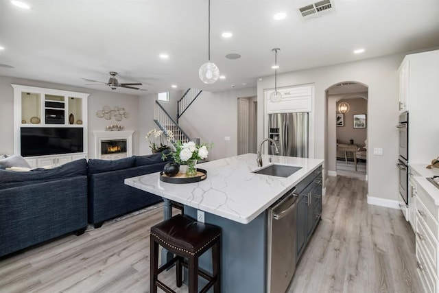 kitchen featuring visible vents, a sink, a glass covered fireplace, arched walkways, and appliances with stainless steel finishes