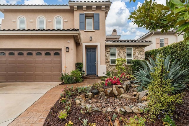 mediterranean / spanish-style home featuring a chimney, stucco siding, concrete driveway, stone siding, and a tile roof