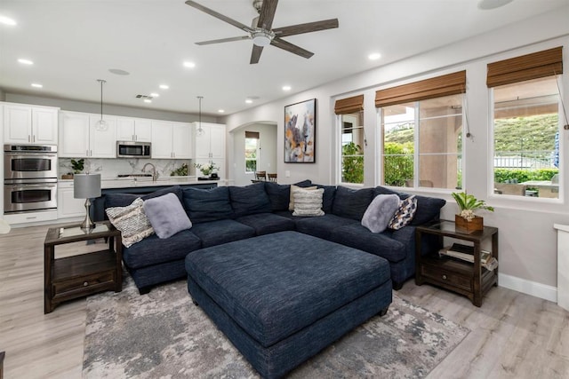 living room featuring a ceiling fan, recessed lighting, arched walkways, light wood-style floors, and baseboards