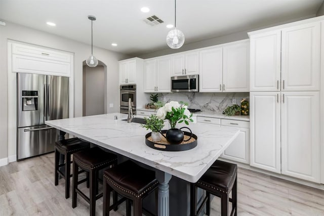 kitchen with pendant lighting, tasteful backsplash, white cabinetry, stainless steel appliances, and arched walkways