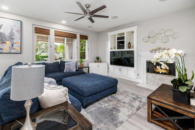 living area featuring a glass covered fireplace, recessed lighting, a ceiling fan, and wood finished floors