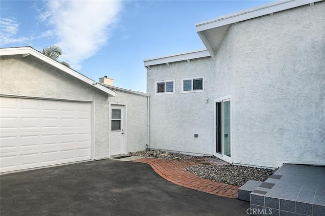 view of property exterior with stucco siding, a chimney, and a garage